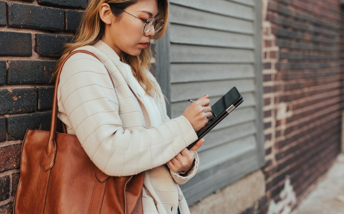 Woman leaning on wall while working on a tablet.