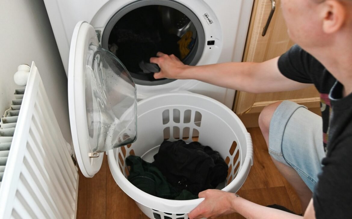 A man is putting clothes into a washing machine.